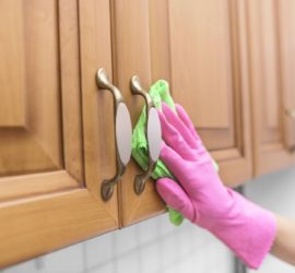 A gloved hand wiping down a cabinet with a cloth.