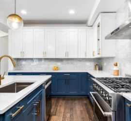 A kitchen with white upper cabinetry and blue lower cabinetry and gold fixtures.