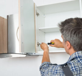 A man using a screwdriver to install a top kitchen cabinet.